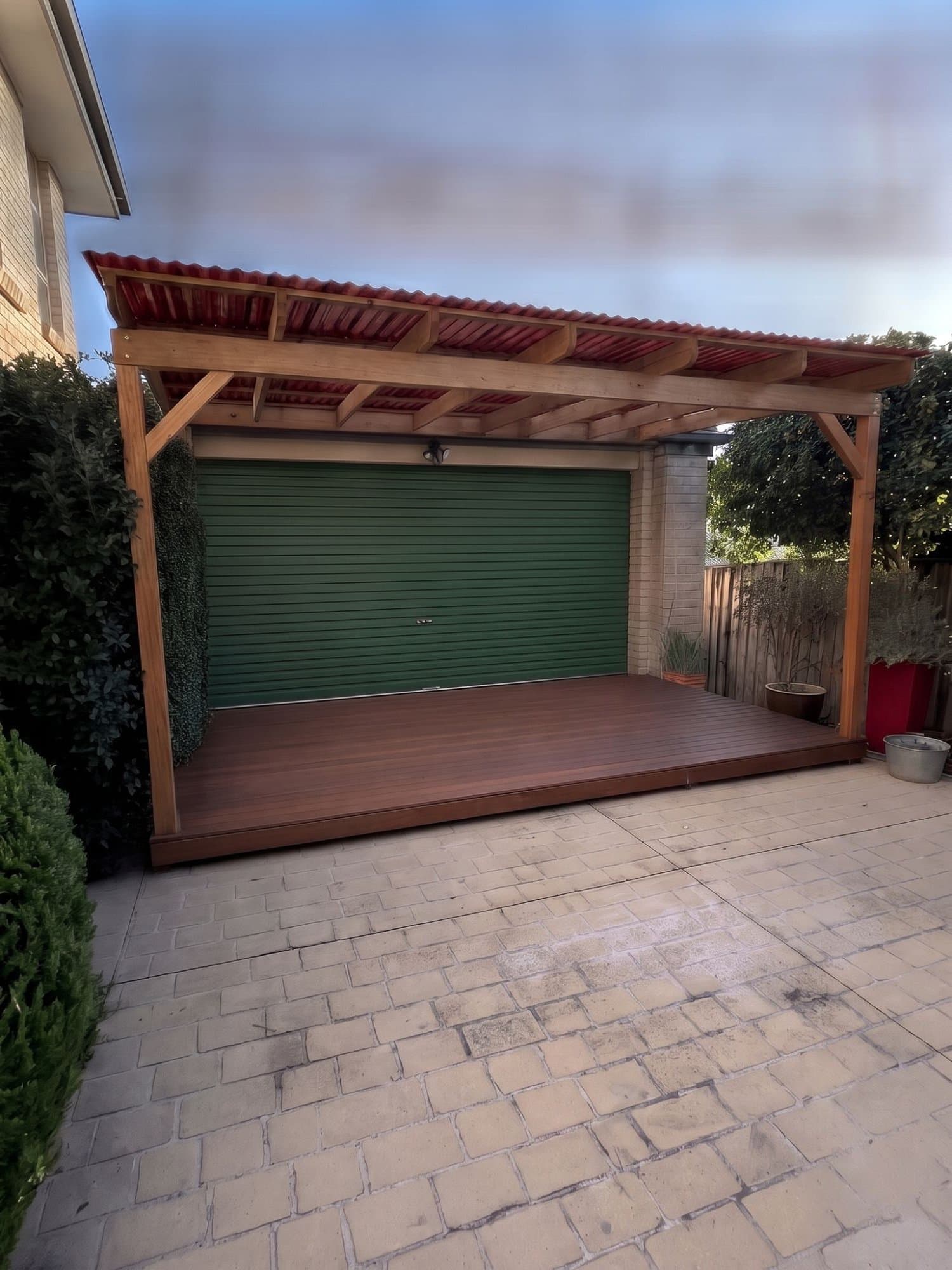 The same driveway rendered with a timber pergola, a raised timber deck and a green garage door.