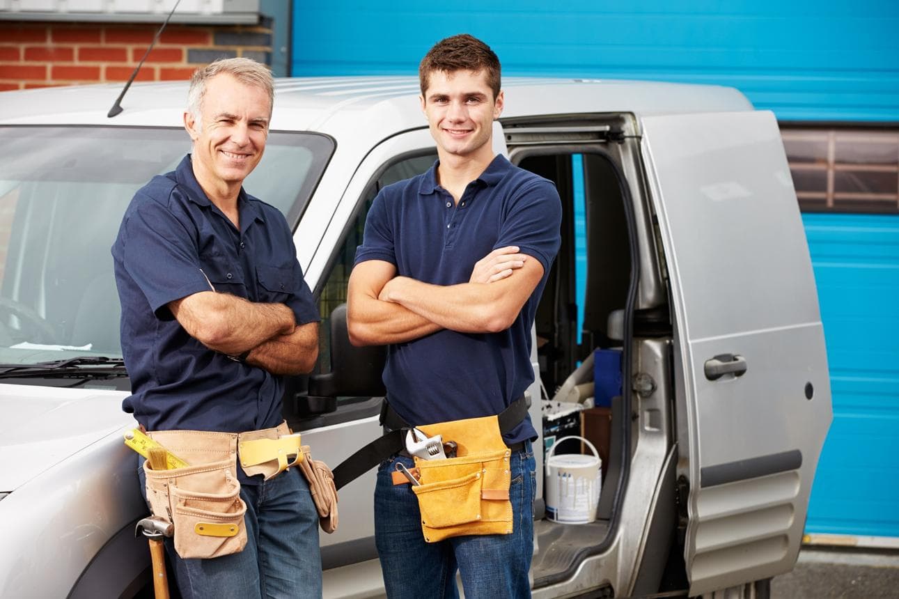 Two tradies in navy work shirts standing in front of their work van.